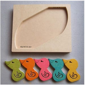 May include: A wooden puzzle featuring a light brown base with a curved cutout and five colorful duck-shaped pieces. The ducks are green, orange, pink, teal, and yellow. The base has the text "http://witful.net".