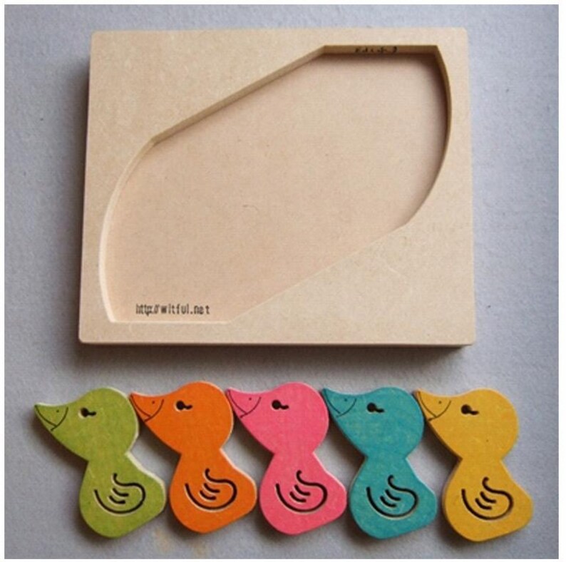 May include: A wooden puzzle featuring a light brown base with a curved cutout and five colorful duck-shaped pieces. The ducks are green, orange, pink, teal, and yellow. The base has the text "http://witful.net".