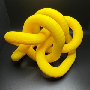 May include: A bright yellow 3D printed knot sculpture. The knot is made of multiple intertwined loops, creating a complex and abstract design.