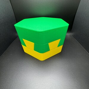 May include: A green and yellow hexagonal box with a lid. The box is made of plastic and has a smooth, glossy finish.