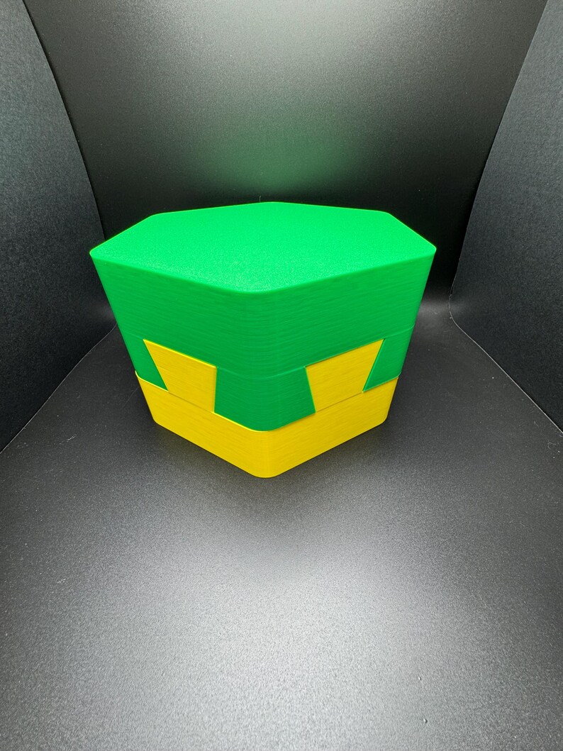 May include: A green and yellow hexagonal box with a lid. The box is made of plastic and has a smooth, glossy finish.