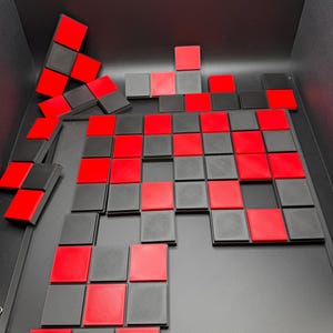 K&ouml;nnte beinhalten: Ein Kachelspiel in Schwarz und Rot, angeordnet in einem Schachbrettmuster. Einige Kacheln sind gestapelt. Das Spiel befindet sich vor einem schwarzen Hintergrund.