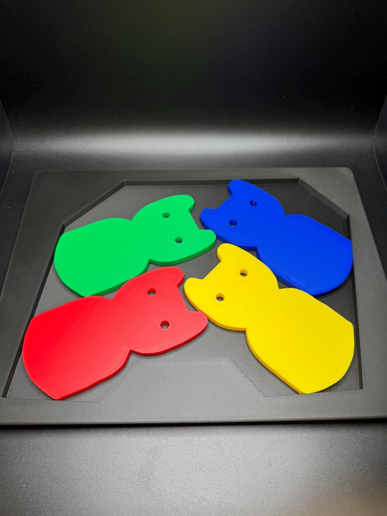 May include: Four colorful cat-shaped acrylic pieces in red, green, blue, and yellow. Each piece has two small holes and is set on a dark gray tray. The shapes are arranged in a playful, eye-catching display.