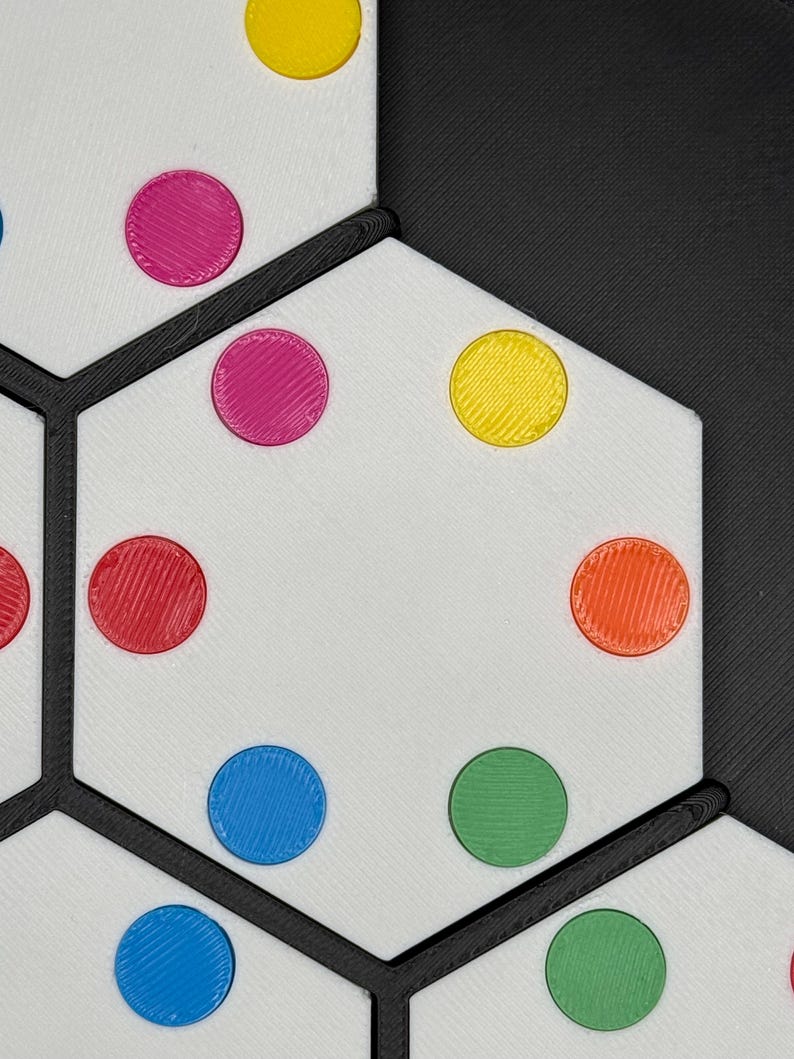 May include: A white hexagonal game board with black lines and colorful circles. The circles are red, pink, yellow, blue, and green.