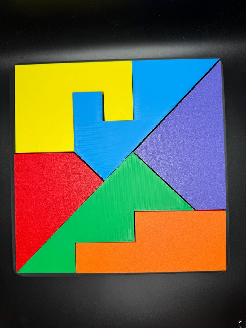 May include: A colorful wooden puzzle with seven pieces in different shapes and colors. The pieces are arranged to form a square. The colors are yellow, blue, green, red, orange, and purple.