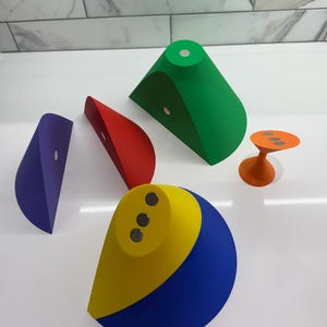 Op de afbeelding: Vijf kleurrijke geometrische vormen met magnetische bases. De vormen zijn een groene kegel, een rode halve cirkel, een paarse halve cirkel, een gele en blauwe halve cirkel en een oranje kegel.