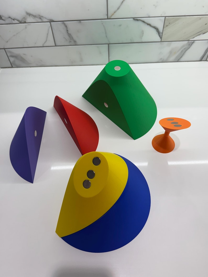 Op de afbeelding: Vijf kleurrijke geometrische vormen met magnetische bases. De vormen zijn een groene kegel, een rode halve cirkel, een paarse halve cirkel, een gele en blauwe halve cirkel en een oranje kegel.