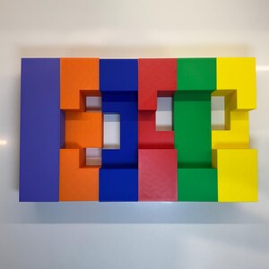 May include: A colorful block puzzle made of six blocks in different colors: purple, orange, blue, red, green, and yellow. The blocks are arranged in a row and have cutouts that create a pattern.