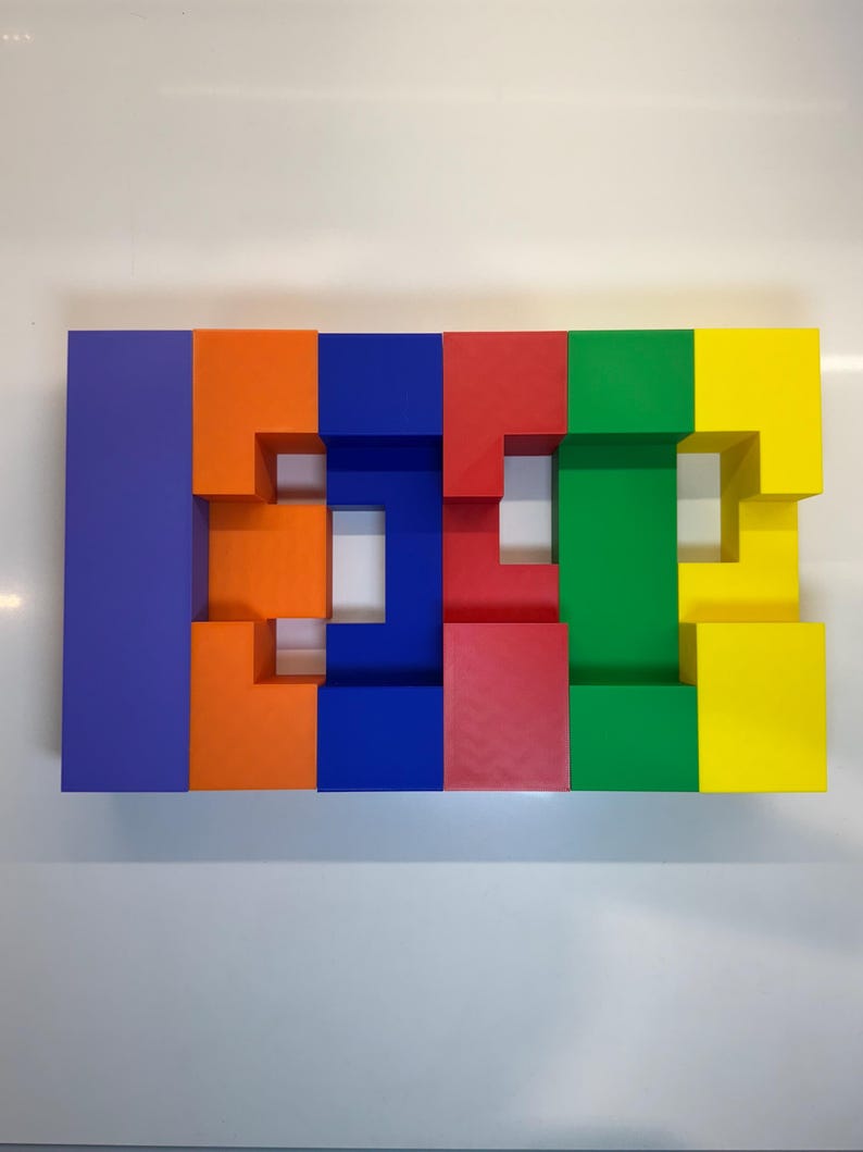 May include: A colorful block puzzle made of six blocks in different colors: purple, orange, blue, red, green, and yellow. The blocks are arranged in a row and have cutouts that create a pattern.