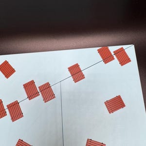 May include: An overhead shot shows a light blue surface with several small, rectangular, reddish-orange objects scattered across it. The objects have a slatted design. Thin black lines are visible on the surface, possibly indicating a grid or pattern.