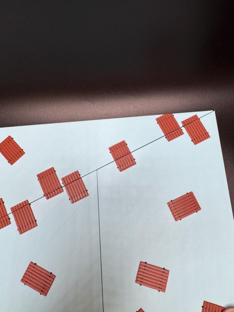 May include: An overhead shot shows a light blue surface with several small, rectangular, reddish-orange objects scattered across it. The objects have a slatted design. Thin black lines are visible on the surface, possibly indicating a grid or pattern.
