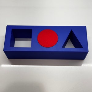 May include: A blue rectangular block with three cutouts: a square, a circle, and a triangle. The circle cutout is filled with a red circle.