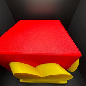 Pode incluir: Um objeto impresso em 3D vermelho e amarelo com uma forma geom&eacute;trica. O objeto tem uma parte superior vermelha e uma base amarela em forma de cora&ccedil;&atilde;o.