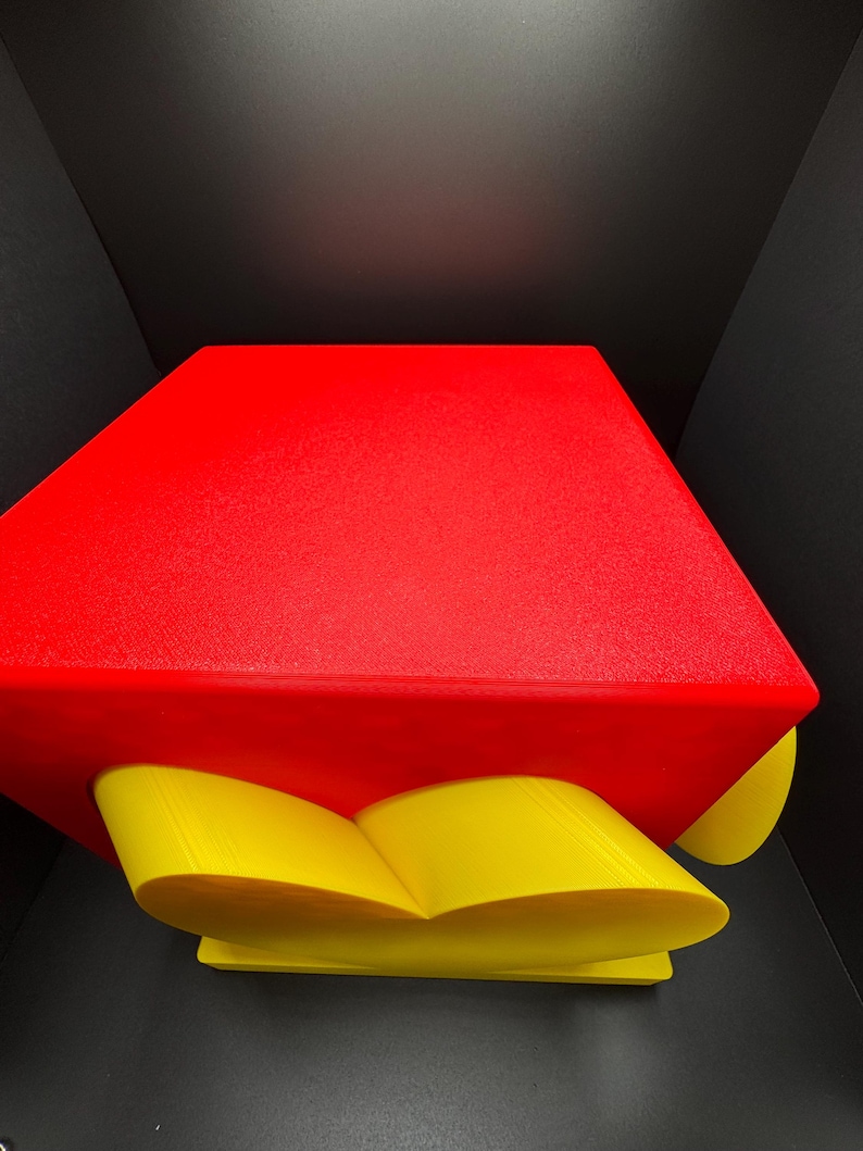 Pode incluir: Um objeto impresso em 3D vermelho e amarelo com uma forma geom&eacute;trica. O objeto tem uma parte superior vermelha e uma base amarela em forma de cora&ccedil;&atilde;o.
