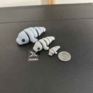 Puede incluir: Tres figuritas de manat&iacute; de arcilla gris de diferentes tama&ntilde;os, la m&aacute;s grande mide aproximadamente 10 cm de largo, la m&aacute;s peque&ntilde;a aproximadamente 2,5 cm de largo, y se incluye una moneda de plata para la escala.