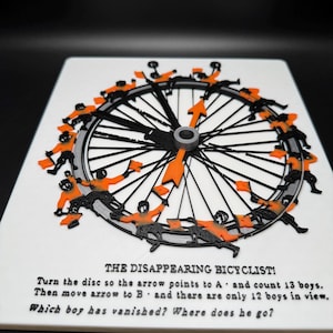 May include: A white circular puzzle with a black wheel and orange flags. The puzzle is titled "The Disappearing Bicyclist!" and includes the text "Turn the disc so the arrow points to A and count 13 boys. Then move arrow to B and there are only 12 boys in view. Which boy has vanished? Where does he go?"