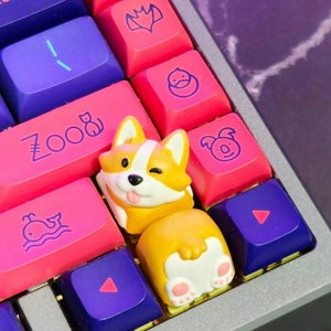 Op de afbeelding: Een aangepast toetsenbord met roze, paarse en blauwe toetsen. Een corgi-vormige toets knipoogt met zijn tong. Andere toetsen hebben dierlijke en geometrische ontwerpen.