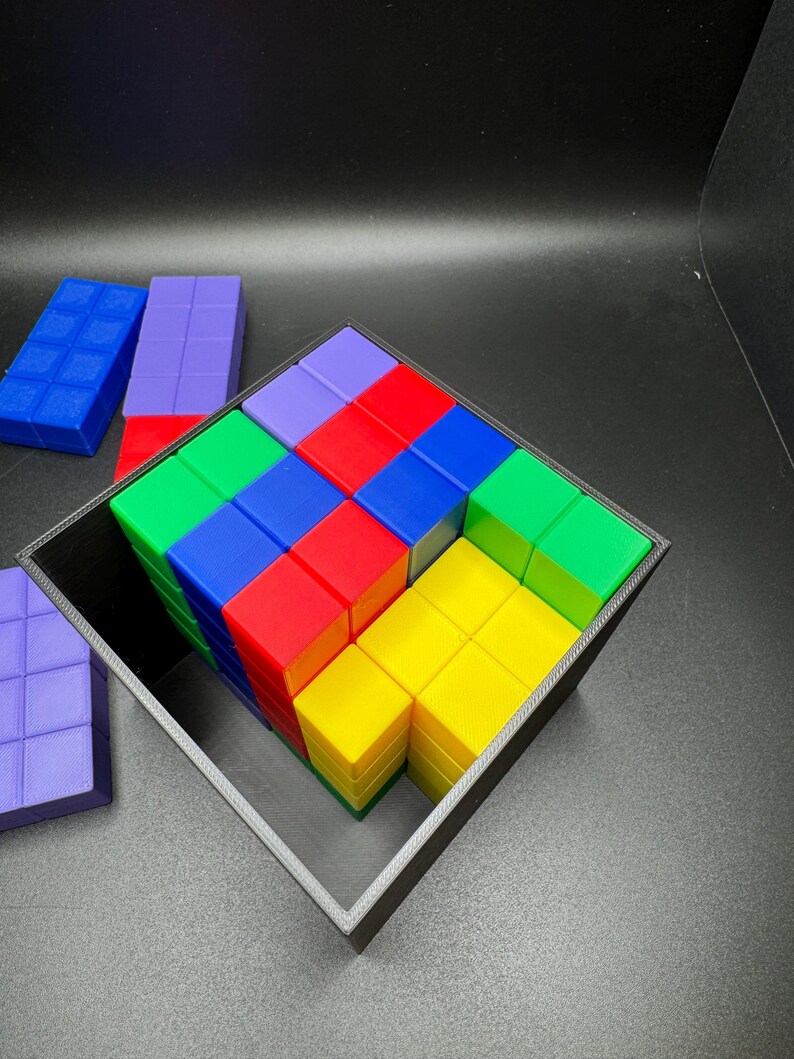 May include: A colorful cube puzzle with a black frame. The puzzle is composed of smaller blocks in various colors, including red, blue, green, yellow, and purple. Additional blocks are visible outside the frame. The background is black.