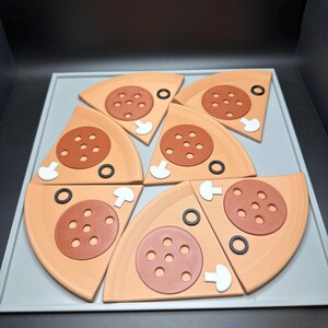 May include: Six triangular pizza slice coasters arranged in a circle. Each slice is light tan with a brown pepperoni topping featuring five holes, a white mushroom slice, and a black olive ring. The coasters are displayed on a light gray tray.