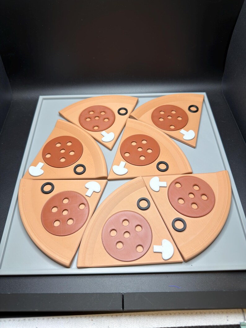 May include: Six triangular pizza slice coasters arranged in a circle. Each slice is light tan with a brown pepperoni topping featuring five holes, a white mushroom slice, and a black olive ring. The coasters are displayed on a light gray tray.