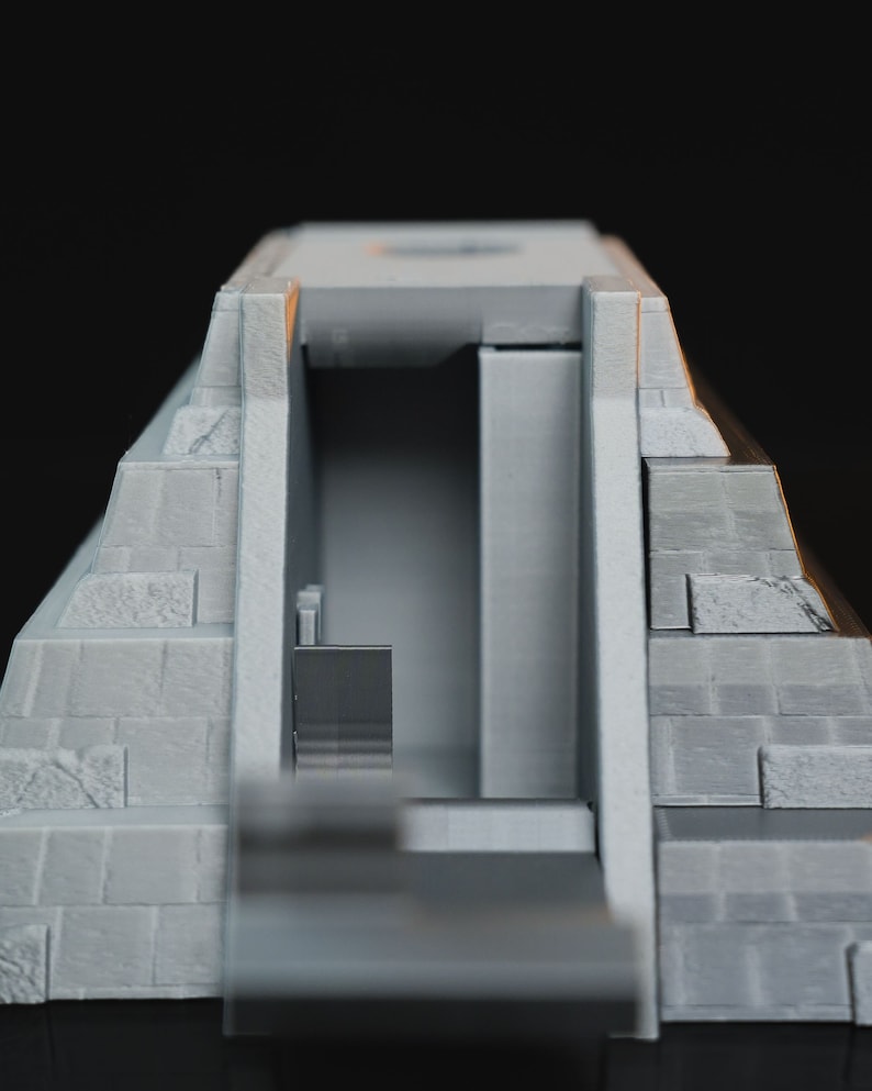 May include: A gray 3D printed model of a pyramid with a doorway and an interior. The pyramid is made of stacked blocks.