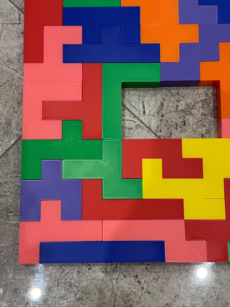 May include: A colourful puzzle made of plastic blocks in various shapes and colours, including red, green, blue, yellow, orange, and purple. The blocks are arranged in a pattern to form a square shape with a small opening in the centre.