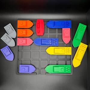 Op de afbeelding: Een set van 15 kleurrijke speelgoedbootjes gerangschikt op een zwart rooster. De bootjes zijn gemaakt van plastic en zijn verkrijgbaar in verschillende kleuren, waaronder rood, blauw, groen, geel en oranje.
