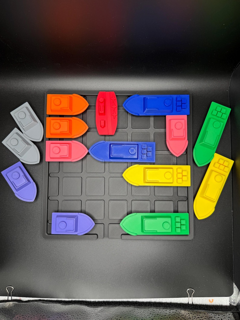 Op de afbeelding: Een set van 15 kleurrijke speelgoedbootjes gerangschikt op een zwart rooster. De bootjes zijn gemaakt van plastic en zijn verkrijgbaar in verschillende kleuren, waaronder rood, blauw, groen, geel en oranje.