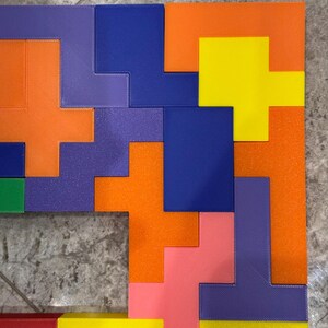 May include: A colourful puzzle made of different shaped pieces. The puzzle is made of orange, yellow, blue, purple, pink, and red pieces. The pieces are arranged in a pattern to form a square.
