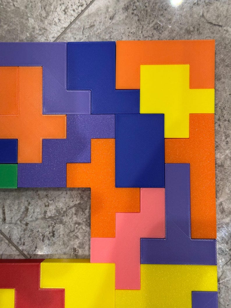 May include: A colourful puzzle made of different shaped pieces. The puzzle is made of orange, yellow, blue, purple, pink, and red pieces. The pieces are arranged in a pattern to form a square.
