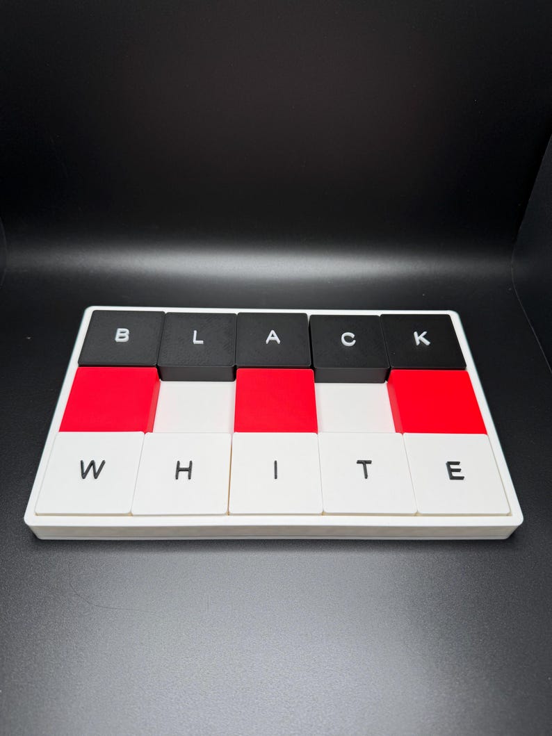 May include: A rectangular puzzle with the words "BLACK WHITE" spelled out in individual letter blocks. The blocks alternate between black, red, and white. The letters are in a sans-serif font.
