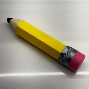 May include: A large yellow pencil with a black eraser and a pink eraser cap. The pencil is made of wood and has a silver band around the eraser.