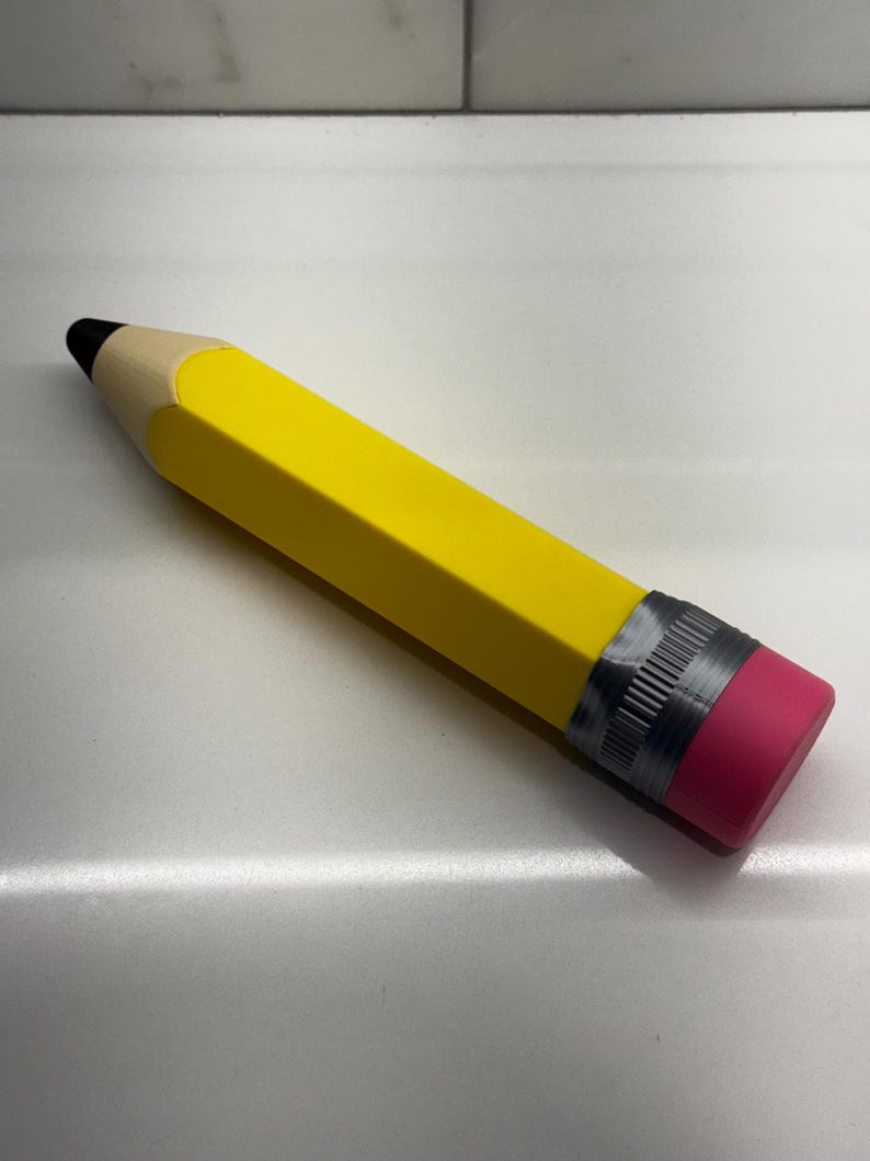 May include: A large yellow pencil with a black eraser and a pink eraser cap. The pencil is made of wood and has a silver band around the eraser.