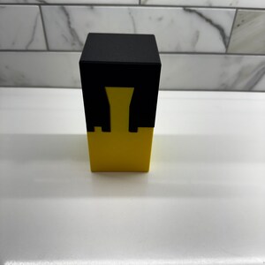 May include: A black and yellow cube puzzle with a hollow center. The puzzle is made of two pieces that fit together.