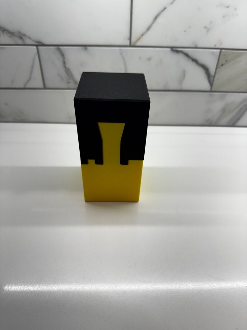 May include: A black and yellow cube puzzle with a hollow center. The puzzle is made of two pieces that fit together.