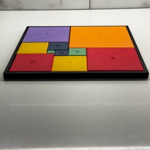 Peut inclure: Un puzzle carr&eacute; color&eacute; avec des carr&eacute;s de diff&eacute;rentes couleurs, chacun avec un num&eacute;ro imprim&eacute; dessus. Les num&eacute;ros sont 5, 33, 19, 12, 7, 23, 16, 35, 21 et 44.