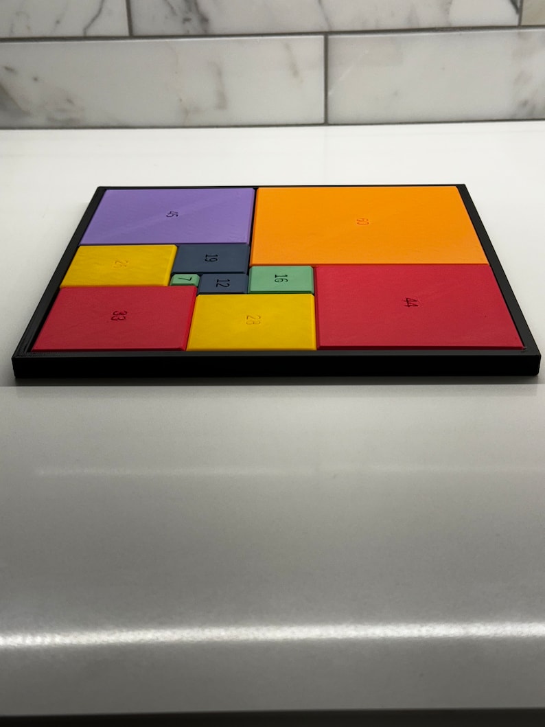 Peut inclure: Un puzzle carr&eacute; color&eacute; avec des carr&eacute;s de diff&eacute;rentes couleurs, chacun avec un num&eacute;ro imprim&eacute; dessus. Les num&eacute;ros sont 5, 33, 19, 12, 7, 23, 16, 35, 21 et 44.
