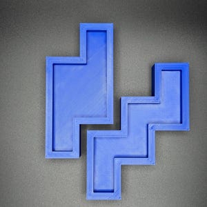 Puede incluir: Un rompecabezas de pl&aacute;stico azul con una forma &uacute;nica, que se asemeja a una combinaci&oacute;n de cuadrados y rect&aacute;ngulos. El rompecabezas est&aacute; formado por dos piezas separadas que encajan.
