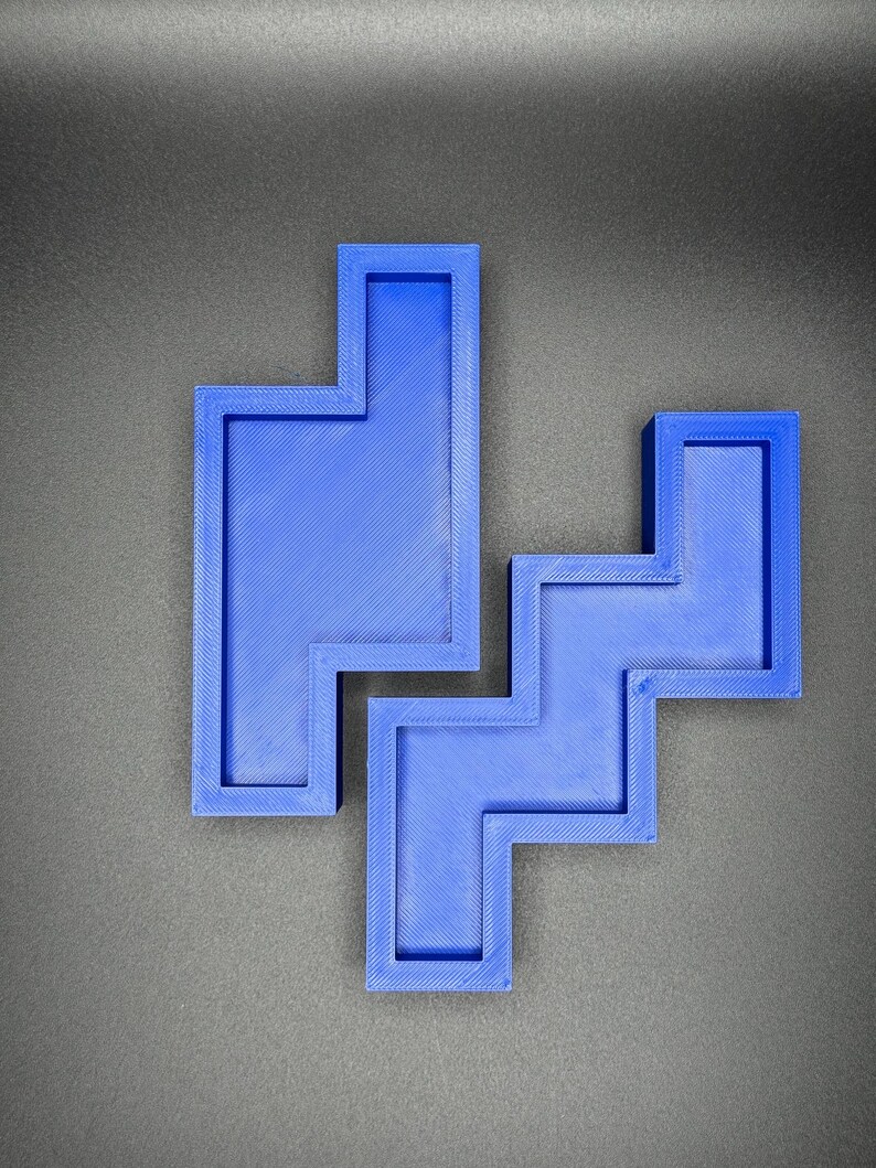 Puede incluir: Un rompecabezas de pl&aacute;stico azul con una forma &uacute;nica, que se asemeja a una combinaci&oacute;n de cuadrados y rect&aacute;ngulos. El rompecabezas est&aacute; formado por dos piezas separadas que encajan.