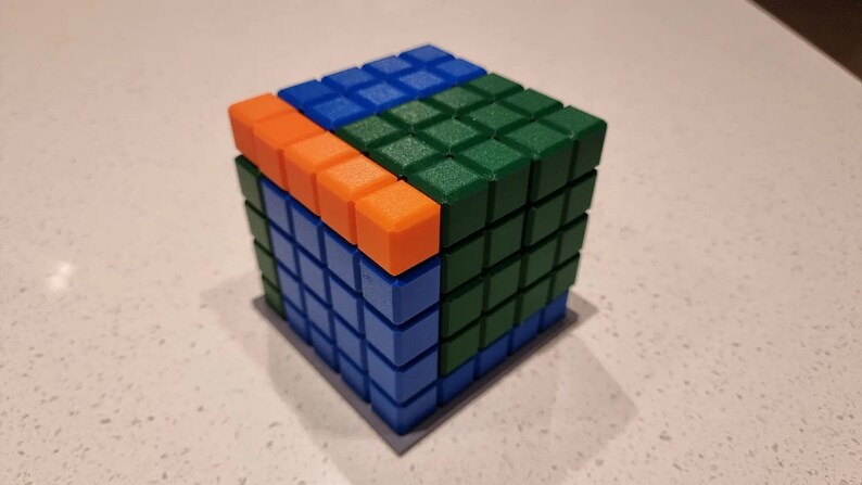 May include: A cube made of small square blocks in blue, green, and orange. The cube is made up of 64 blocks.