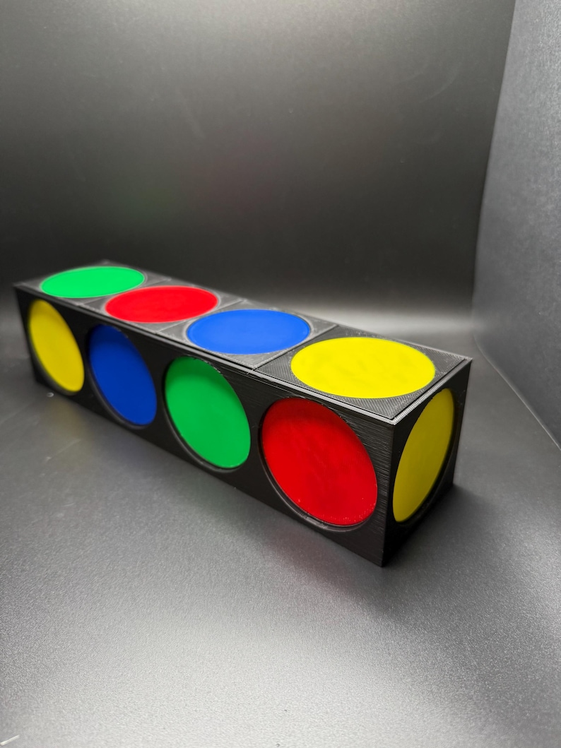 May include: A black rectangular box with six circular openings, each filled with a different colour: yellow, green, red, blue, green, and yellow. The box is on a dark surface.