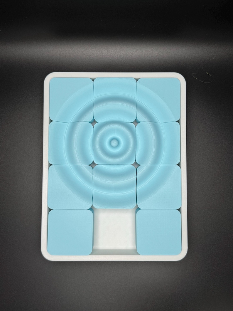 May include: A white tray with a blue puzzle inside. The puzzle is made up of nine square tiles with a concentric circle design.