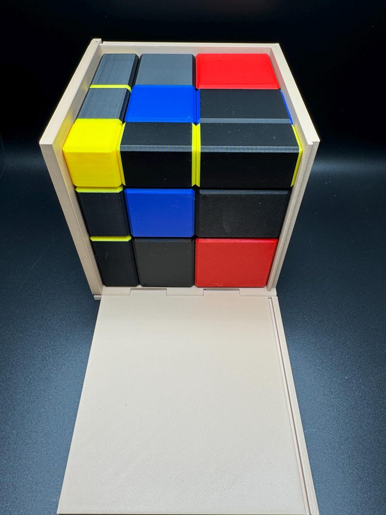 May include: A wooden box with a sliding lid, containing a 3x3 cube puzzle made of small blocks in red, blue, yellow, black, and grey.