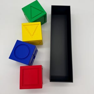 May include: Four colorful blocks with different geometric shapes on each side. The blocks are stacked on top of each other. A black rectangular box is next to the blocks.