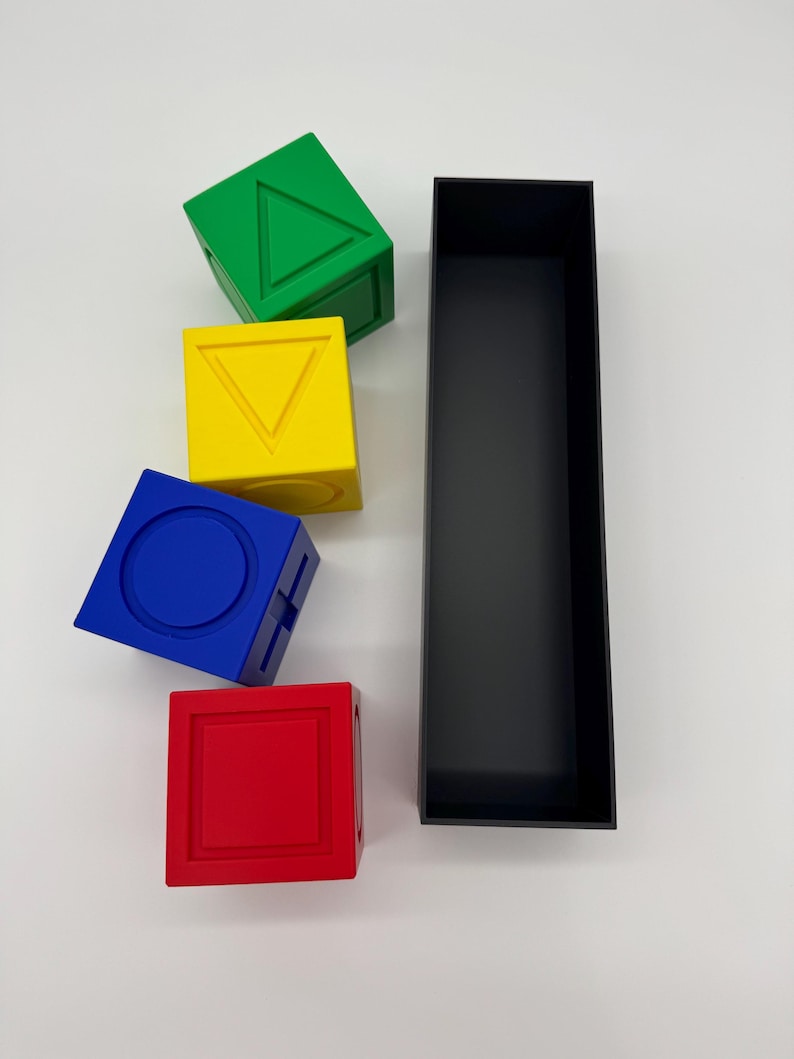 May include: Four colorful blocks with different geometric shapes on each side. The blocks are stacked on top of each other. A black rectangular box is next to the blocks.