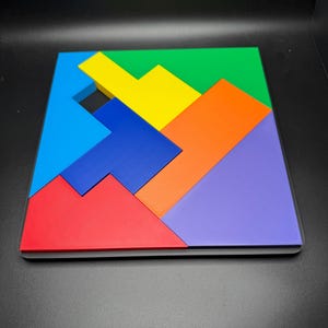 May include: A colorful wooden puzzle with seven pieces in various shapes and sizes. The pieces are arranged to form a square, with the colors red, blue, green, yellow, orange, and purple.