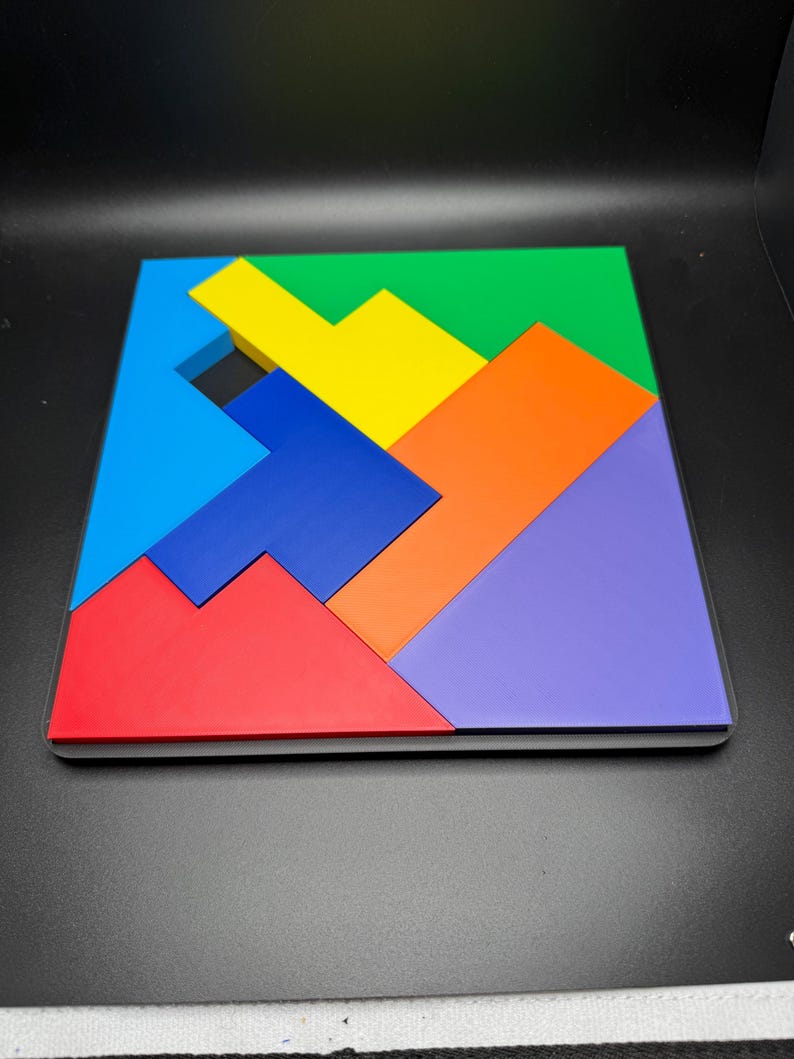 May include: A colorful wooden puzzle with seven pieces in various shapes and sizes. The pieces are arranged to form a square, with the colors red, blue, green, yellow, orange, and purple.