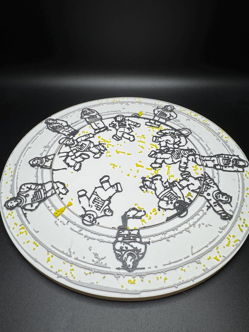 Puede incluir: Un plato de cer&aacute;mica blanco con un dise&ntilde;o gris y amarillo. El plato presenta un patr&oacute;n circular de astronautas en contornos negros. El borde del plato tiene un borde gris y est&aacute; salpicado de puntos amarillos.