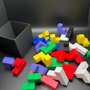 May include: A collection of colorful, geometric puzzle pieces in various shapes and colors, including red, blue, green, yellow, and white. A black square box is in the background. The pieces are scattered on a dark surface.