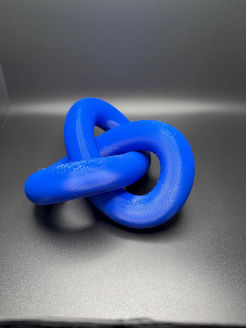 May include: A blue, three-dimensional knot sculpture made of plastic. The knot is a simple, continuous loop that is tied in a way that creates a complex and interesting shape.